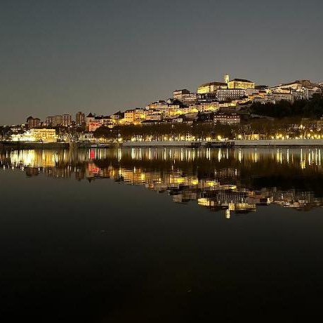 The hill of Coimbra lit up at night, reflected in the river